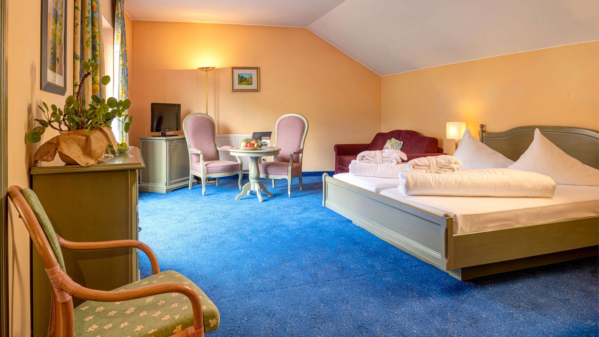 Our family hotel in Tyrol with a 4-star superior rating Hotel room with blue carpet, double bed, seating area, and yellow walls