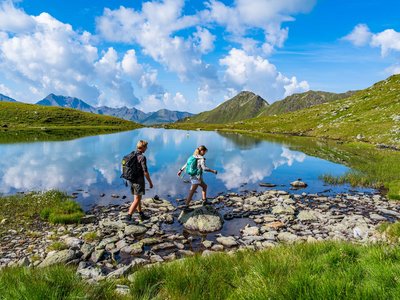 Trekking in Tirolo, Austria: allo Jesacherhof Due escursionisti attraversano un lago roccioso in montagna con cielo limpido
