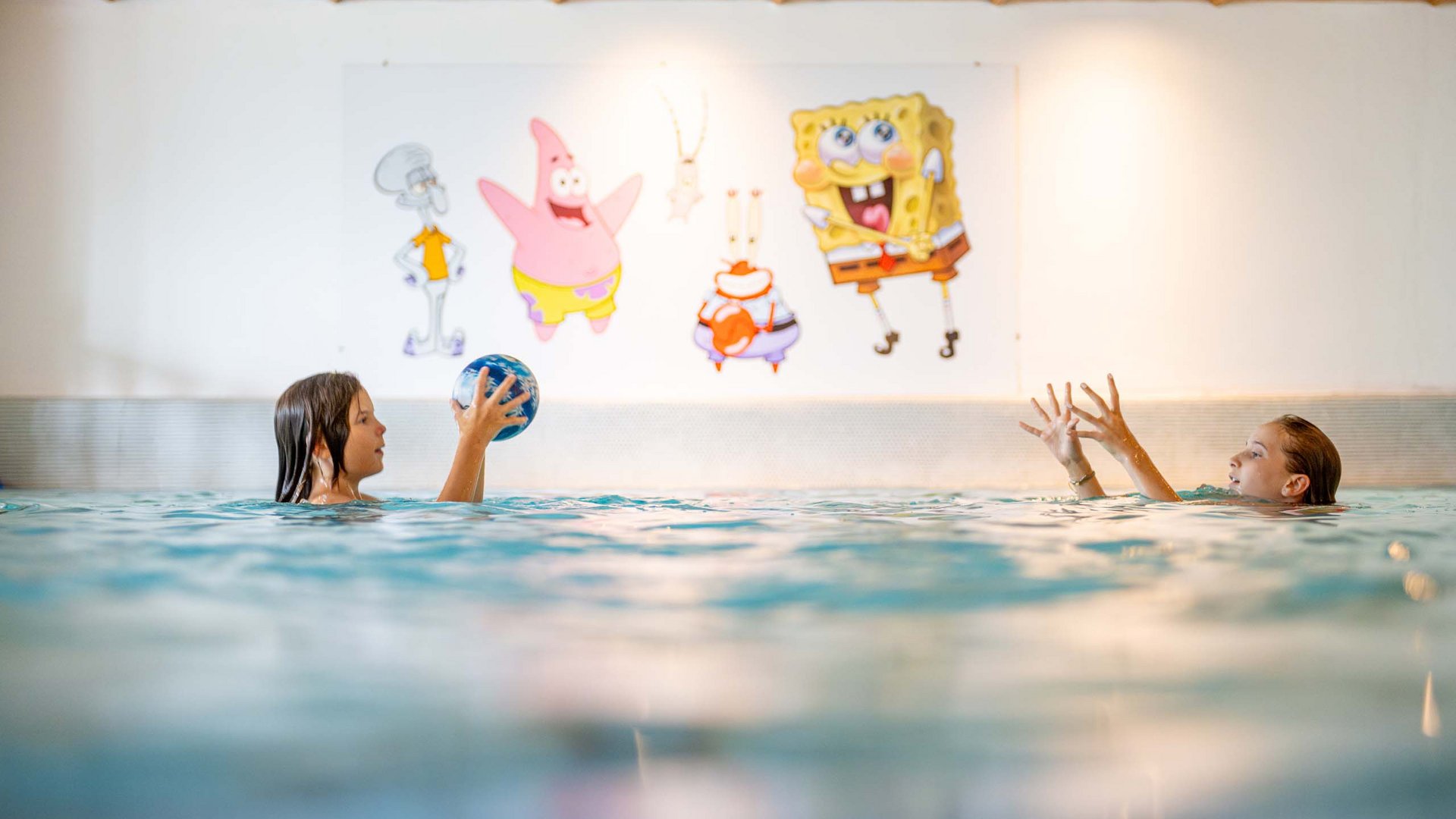 Jesacherhof: Ihr Hotel im Defereggental Zwei Kinder spielen mit Ball im Schwimmbad vor SpongeBob-Wandbild