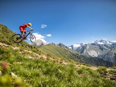 Alpine Urkraft im 4-Sterne-Superior-Hotel in Osttirol Mountainbiker springt im alpinen Gelände vor Bergkulisse