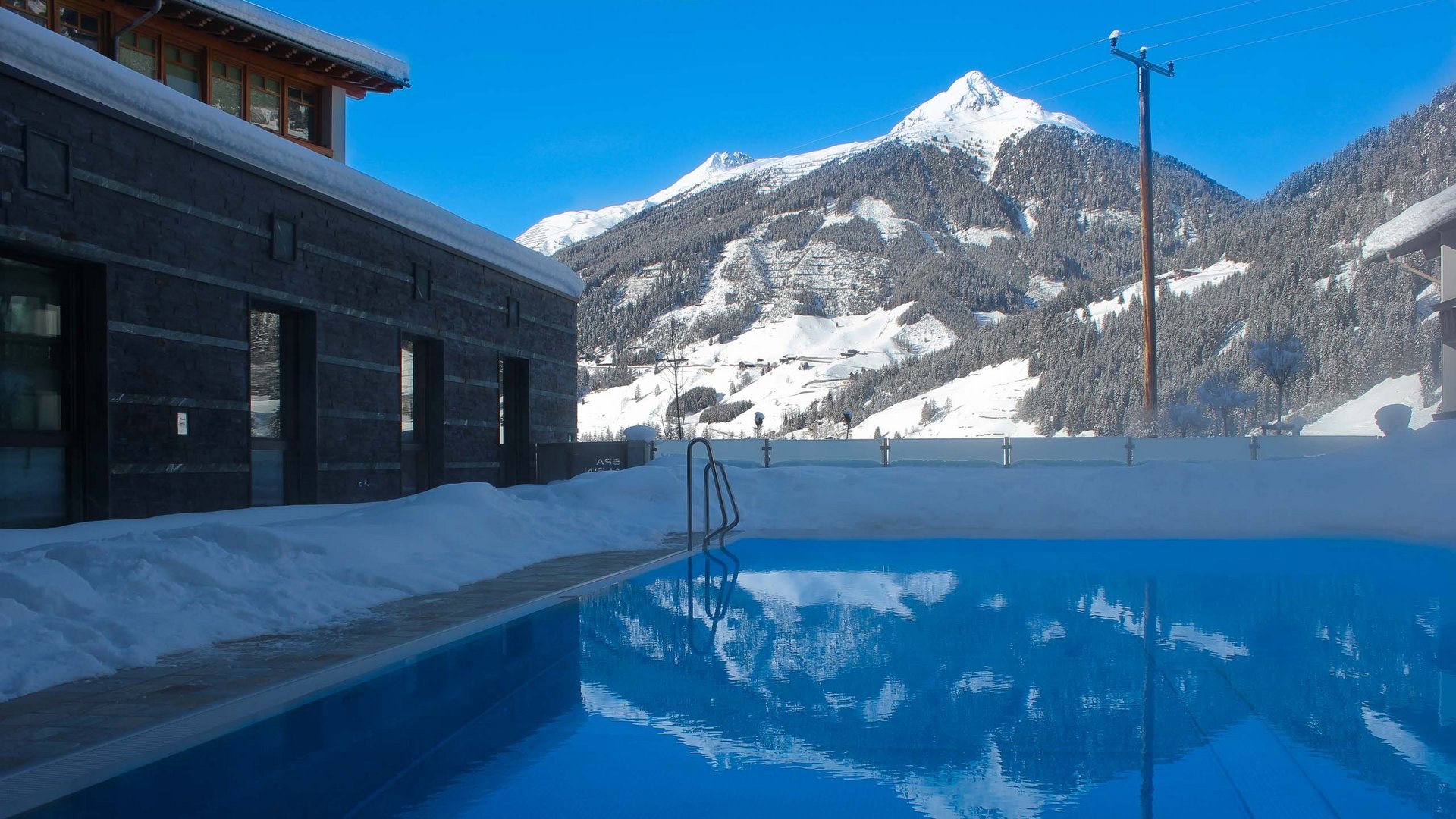 I servizi del nostro hotel per famiglie in Tirolo Piscina all'aperto con vista sulle montagne innevate e cielo azzurro