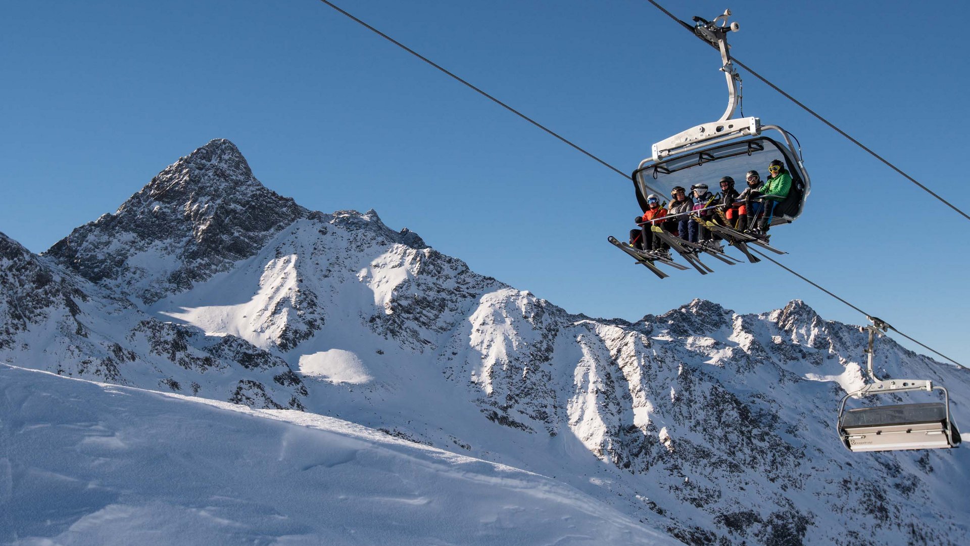 Family hotel in East Tyrol: the Jesacherhof Ski lift with skiers in front of snowy mountains and clear blue sky