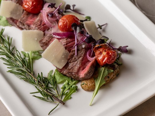 Jesacherhof: Gourmethotel in Österreich Garnierte Rindfleischscheiben mit Tomaten, Rucola und Käse auf weißem Teller