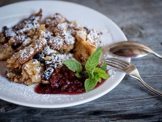 Jesacherhof: Gourmethotel in Österreich Kaiserschmarrn mit Puderzucker, Beerenkompott und Minzblatt auf weißem Teller