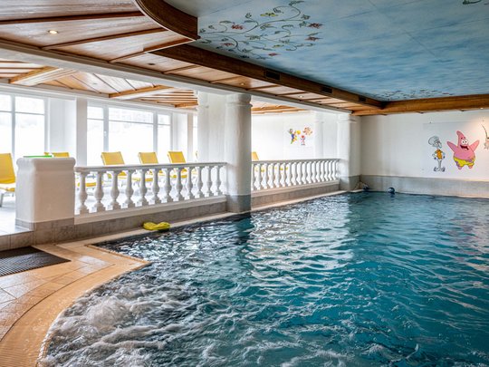 Wellnesshotel im Defereggental: Wohlfühlurlaub vom Feinsten Innenpool mit Wasserspielen und gelben Liegestühlen neben Cartoon-Wandbildern
