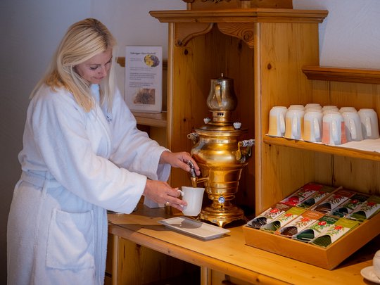 Wellnesshotel im Defereggental: Wohlfühlurlaub vom Feinsten Frau in Bademantel zapft Tee an einem traditionellen Samowar