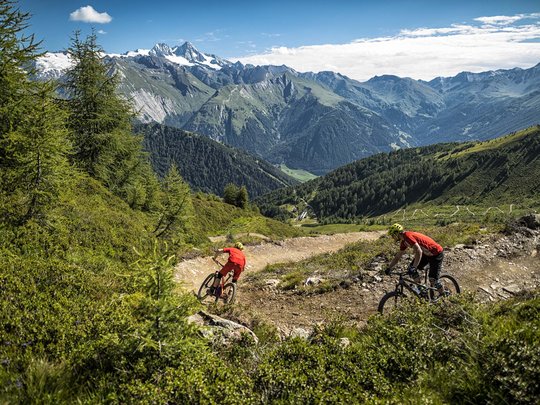 Mountain biking routes for all levels Two mountain bikers on trail with alpine mountain view in background