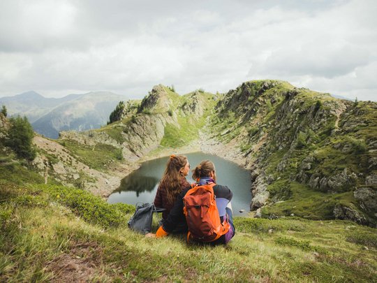 Ausflugsziele im Defereggental Zwei Wanderer sitzen auf einer Wiese mit Blick auf einen Bergsee