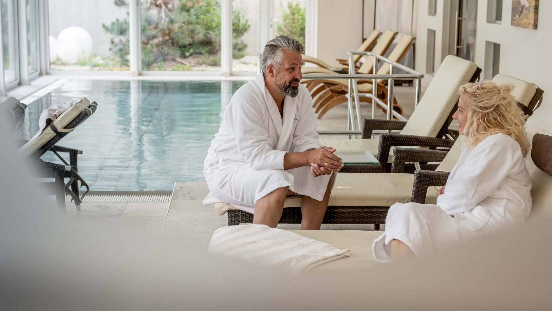 I servizi del nostro hotel per famiglie in Tirolo Uomo e donna in accappatoi vicino a una piscina interna su lettini
