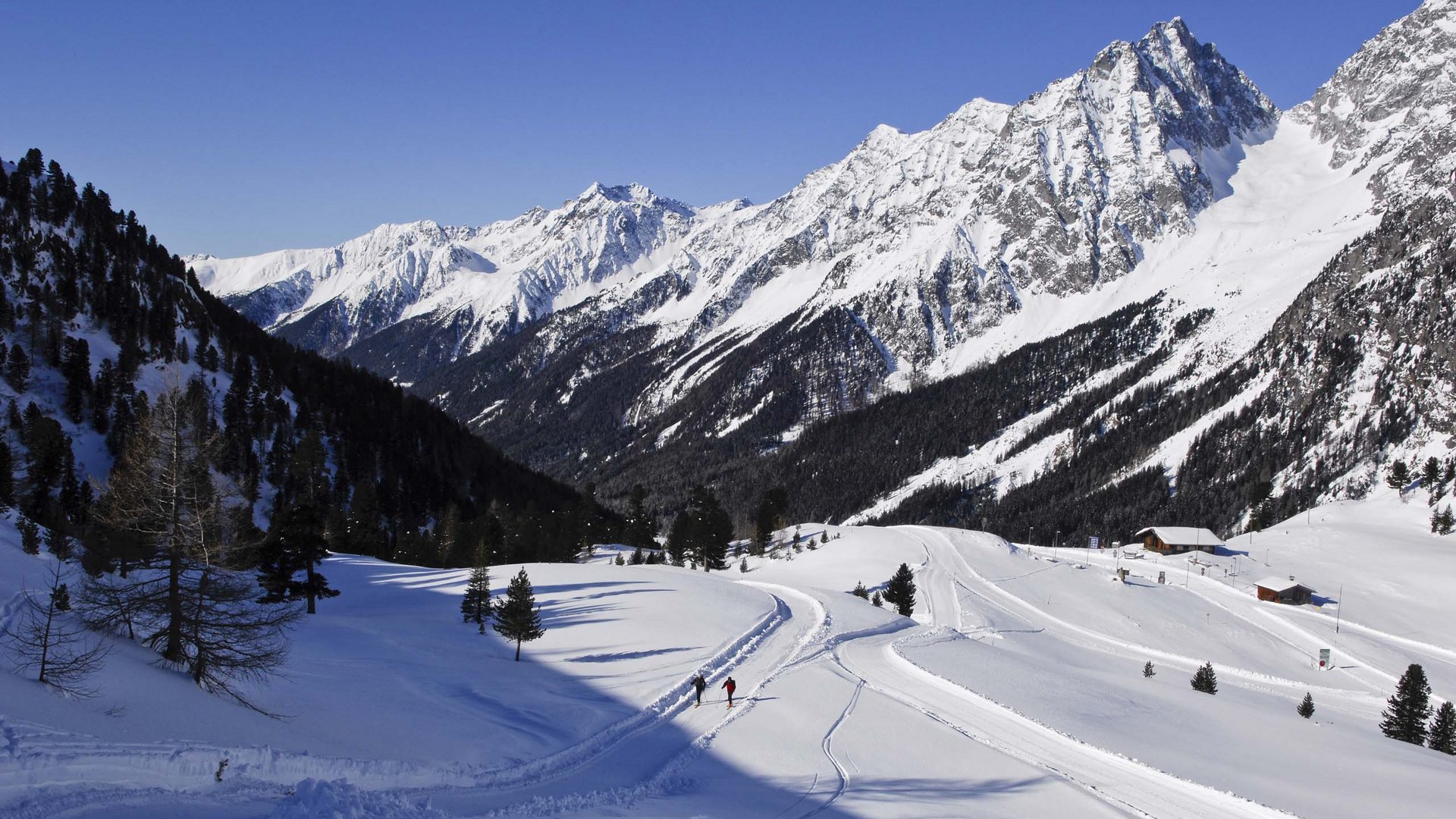 Benessere alpino al nostro albergo in Tirolo Montagne innevate con due sciatori su sentiero in valle alpina