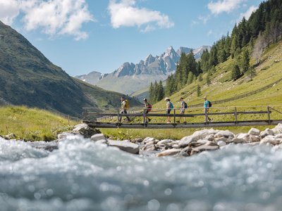 Unsere Tipps für einen Wanderurlaub in Osttirol Gruppe von Wanderern auf einer Brücke in bergiger Landschaft mit Fluss
