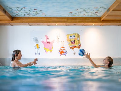 Wellnesshotel im Defereggental: Wohlfühlurlaub vom Feinsten Zwei Kinder spielen mit einem Ball im Hallenbad vor SpongeBob-Wandbild
