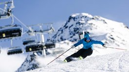 I servizi del nostro hotel per famiglie in Tirolo Sciatore con giacca blu scende velocemente su pista innevata con montagna sullo sfondo