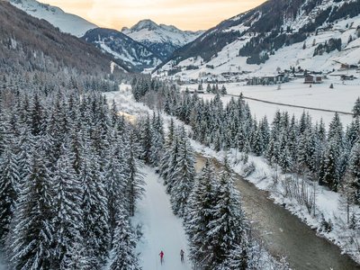 Benessere alpino al nostro albergo in Tirolo Due sciatori di fondo su sentiero innevato tra gli alberi in valle al tramonto