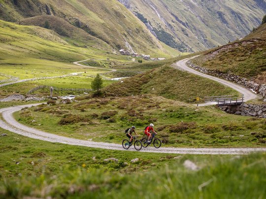 Mountain biking routes for all levels Two mountain bikers on a winding mountain trail in a green landscape