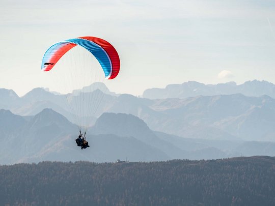 Trekking in Tirolo, Austria: allo Jesacherhof Due persone in parapendio rosso e blu volano sopra montagne boschive