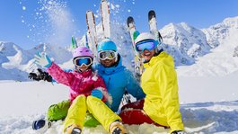 I servizi del nostro hotel per famiglie in Tirolo Famiglia con abbigliamento da sci colorato che gioca nella neve di fronte alle montagne