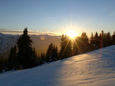 Gourmethotel in Osttirol mit Panoramabar Sonnenuntergang über schneebedecktem Hang und Nadelbäumen in den Bergen
