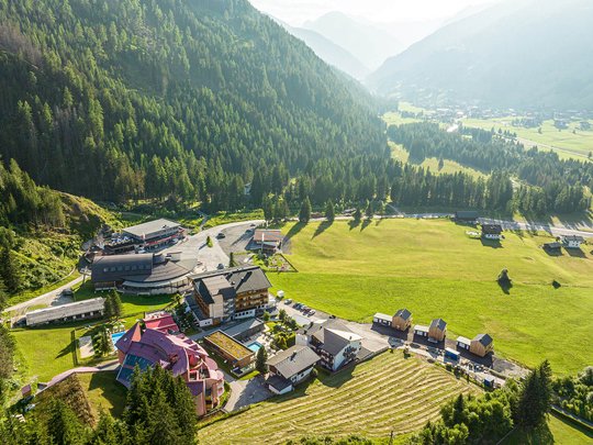 Wanderhotel in Osttirol mit Herz Luftaufnahme eines Bergdorfs mit Wäldern und Wiesen im Sonnenlicht