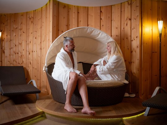 Wellnesshotel im Defereggental: Wohlfühlurlaub vom Feinsten Paar in weißen Bademänteln entspannt sich in einer Sauna mit Holzvertäfelung.