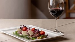 I servizi del nostro hotel per famiglie in Tirolo Carne di manzo con pomodorini e formaggio su piatto accanto a bicchiere di vino rosso