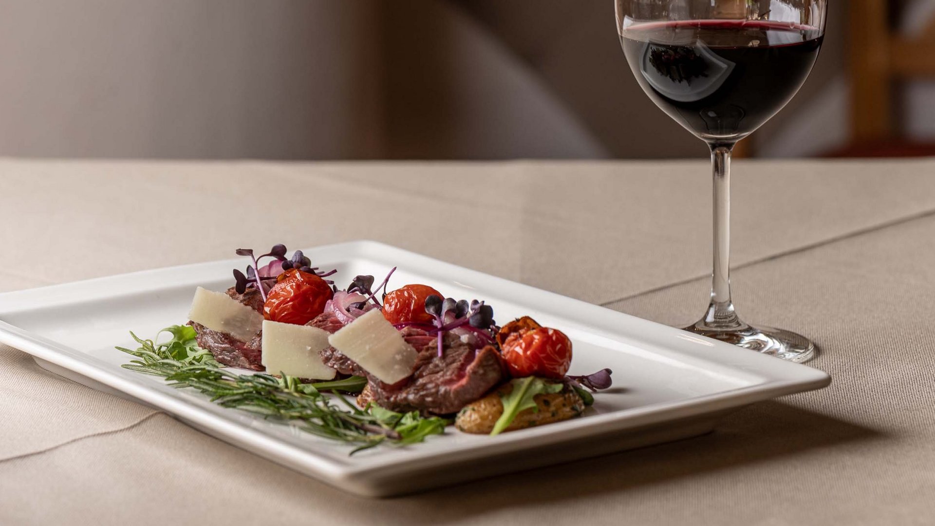 Jesacherhof: Gourmethotel in Österreich Rindfleisch mit Kirschtomaten und Käse auf Teller neben Glas Rotwein