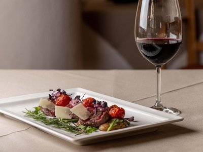 Benessere alpino al nostro albergo in Tirolo Carne di manzo con pomodorini e formaggio su piatto accanto a bicchiere di vino rosso
