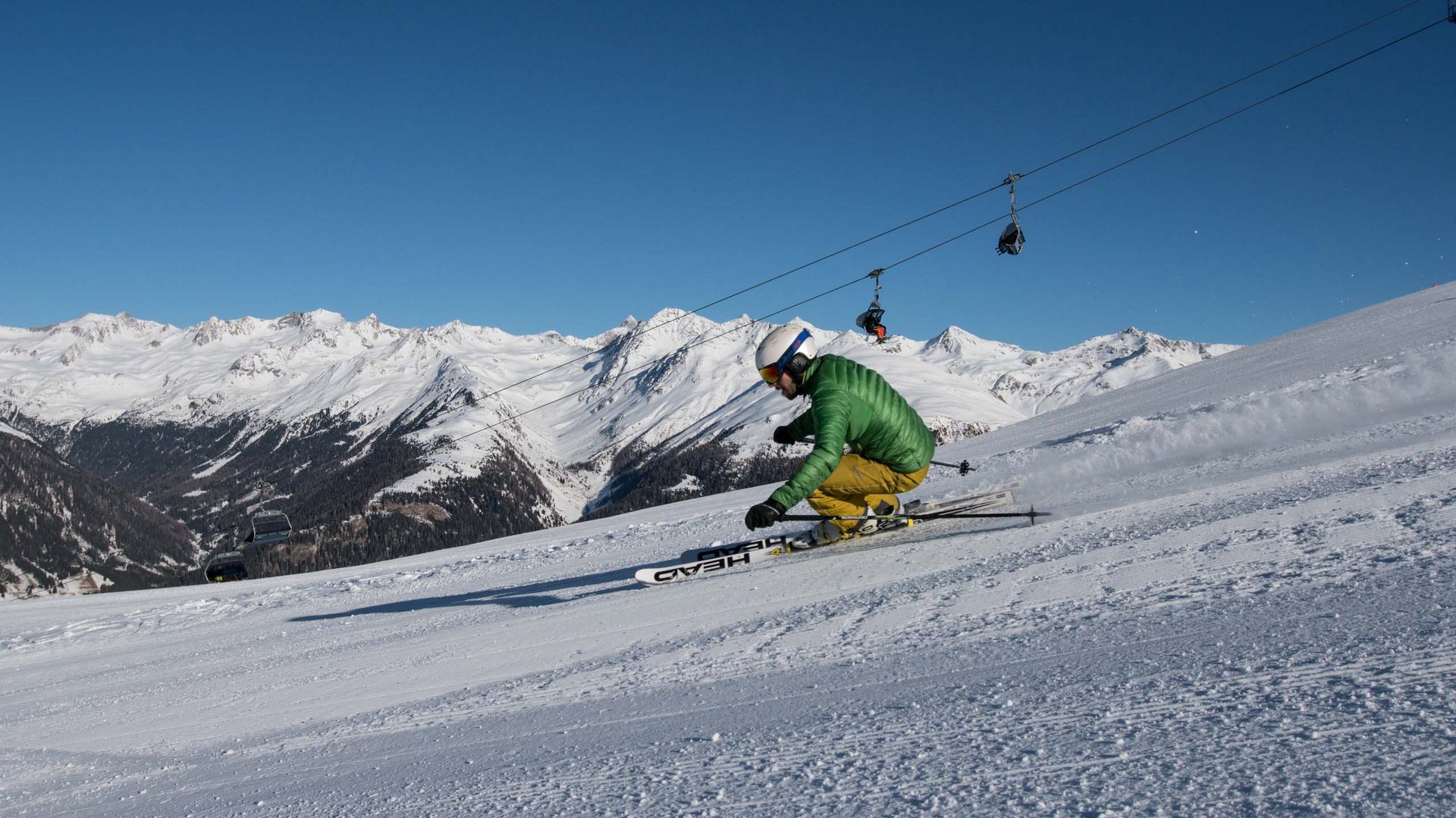 Unvergesslicher Skiurlaub im Defereggental Skifahrer in grüner Jacke und gelber Hose beim Kurvenfahren auf verschneiter Piste