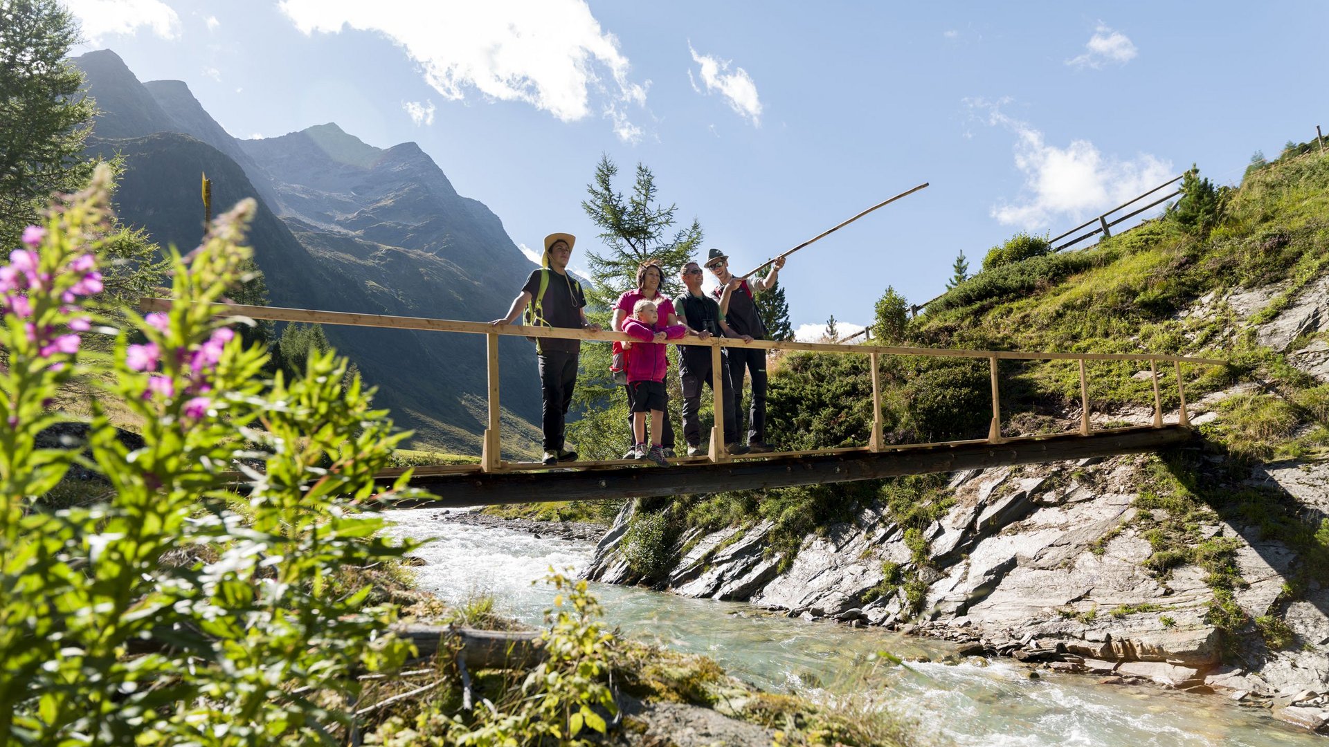 Ausflugsziele im Defereggental Familie auf einer Holzbrücke über einem Gebirgsbach mit Bergen im Hintergrund