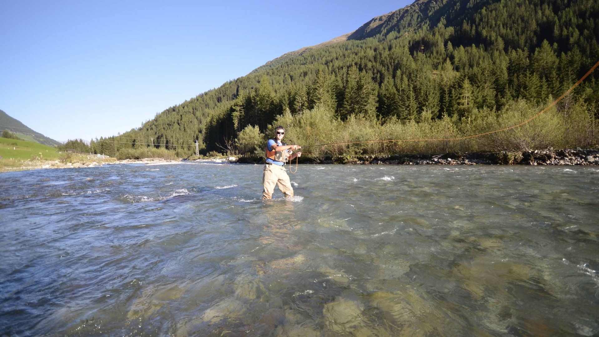 Unvergesslicher Skiurlaub im Defereggental Person angelt in einem glasklaren Fluss vor bewaldetem Berghang
