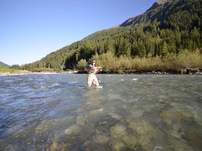 Trekking in Tirolo, Austria: allo Jesacherhof Persona che pesca in un fiume limpido davanti a una montagna boscosa