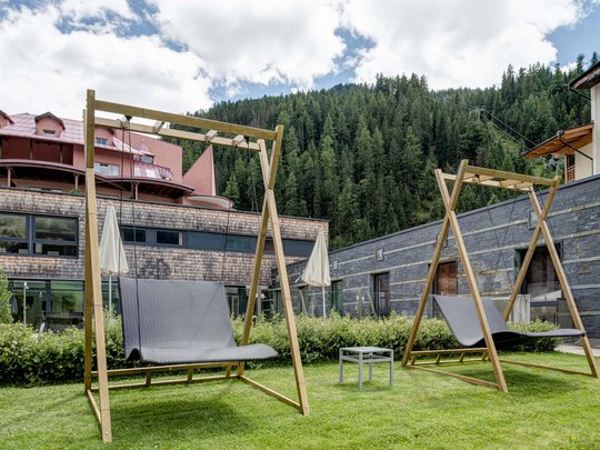 Wellnesshotel im Defereggental: Wohlfühlurlaub vom Feinsten Zwei moderne Holzschaukeln auf einer Rasenfläche vor Gebäuden und Wald