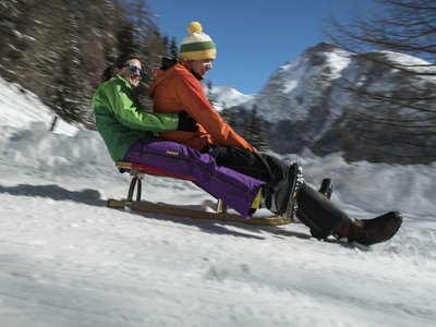 Slittino in Austria. Divertimento in formato famiglia. Due persone che slittano insieme sulla neve con montagne sullo sfondo