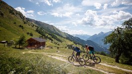 I servizi del nostro hotel per famiglie in Tirolo Due ciclisti su sentiero di montagna con baita e paesaggio alpino