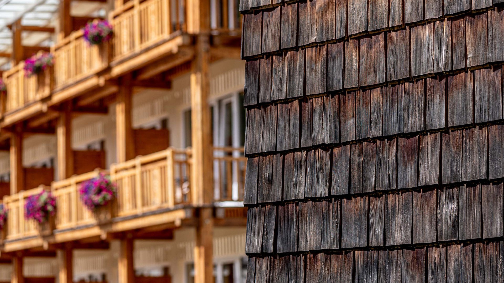 Alpine Urkraft im 4-Sterne-Superior-Hotel in Osttirol Nahaufnahme von verwitterten Holzschindeln an einem Gebäude mit Holzbalkonen im Hintergrund