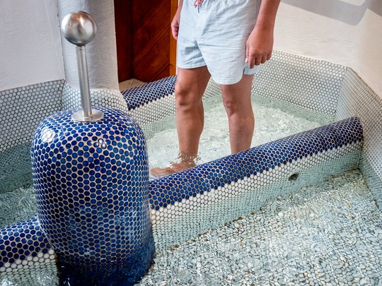 Wellnesshotel im Defereggental: Wohlfühlurlaub vom Feinsten Person steht im Kneippbecken mit blauen Kacheln und Wasser bis zu den Waden