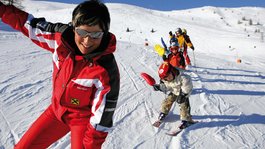 I servizi del nostro hotel per famiglie in Tirolo Istruttrice di sci davanti a un gruppo di bambini che salutano sulla neve