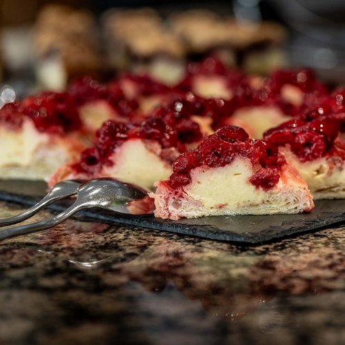 Jesacherhof: Gourmethotel in Österreich Stücke von Käsekuchen mit rotem Beerenbelag auf schwarzer Platte