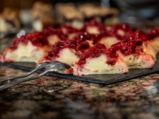 Jesacherhof: Gourmethotel in Österreich Stücke von Käsekuchen mit rotem Beerenbelag auf schwarzer Platte