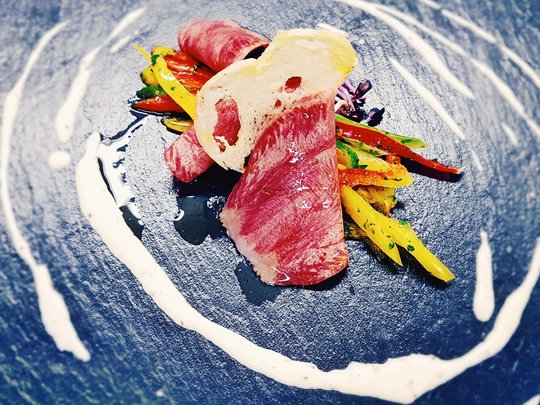 Benessere alpino al nostro albergo in Tirolo Fettine sottili di carne cruda con verdure e salsa su piatto nero