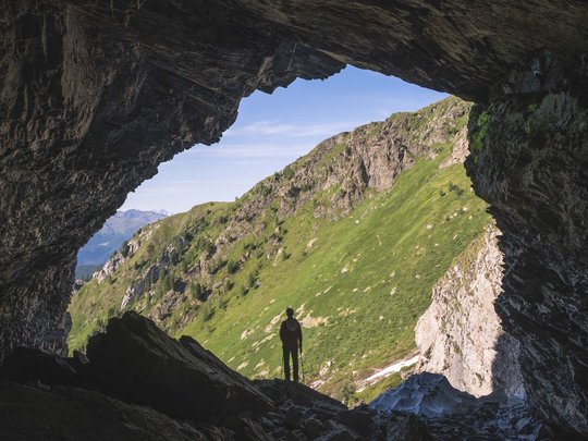 Ausflugsziele im Defereggental Wanderer steht in Höhle mit Blick auf grüne Berglandschaft