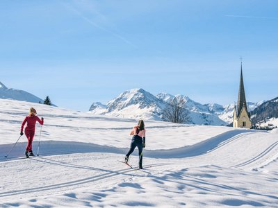An idyllic cross-country skiing area in Austria Two women cross-country skiing with snowy mountains and church in background