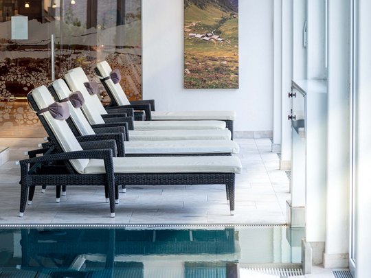 Wellnesshotel im Defereggental: Wohlfühlurlaub vom Feinsten Liegestühle mit weißen Kissen neben einem Hallenbad in einem Wellnessbereich