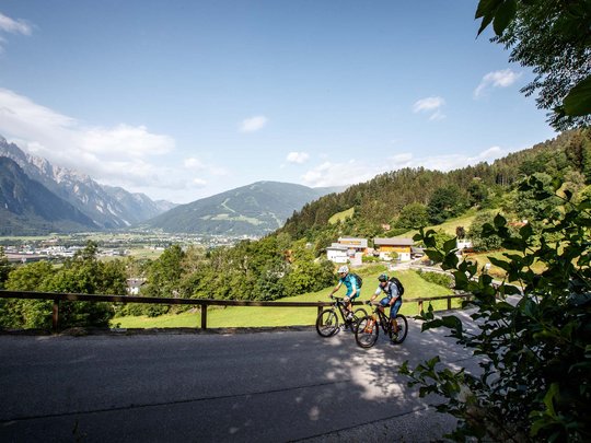 Mountain biking routes for all levels Two cyclists on a mountain road overlooking a valley and mountains