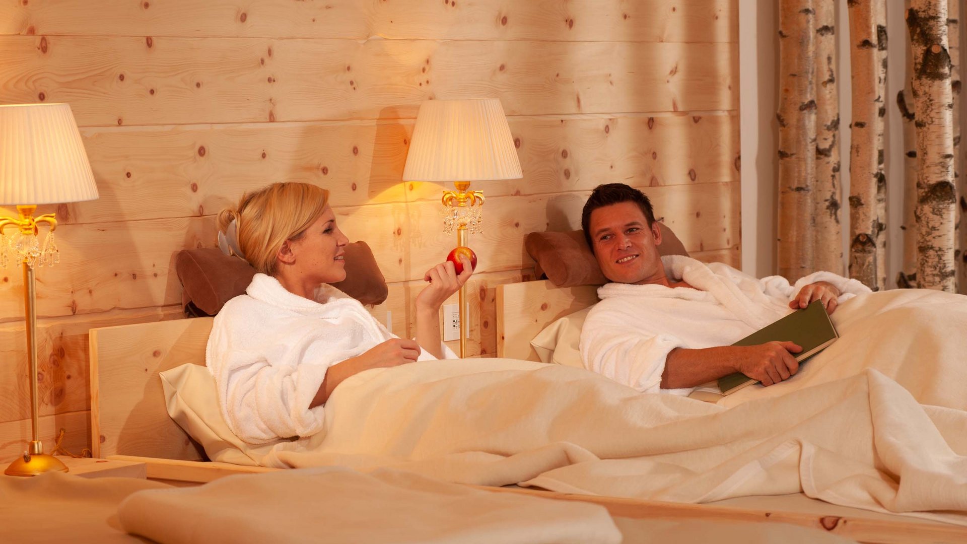Benessere alpino al nostro albergo in Tirolo Coppia in accappatoi rilassata in camera da letto in legno