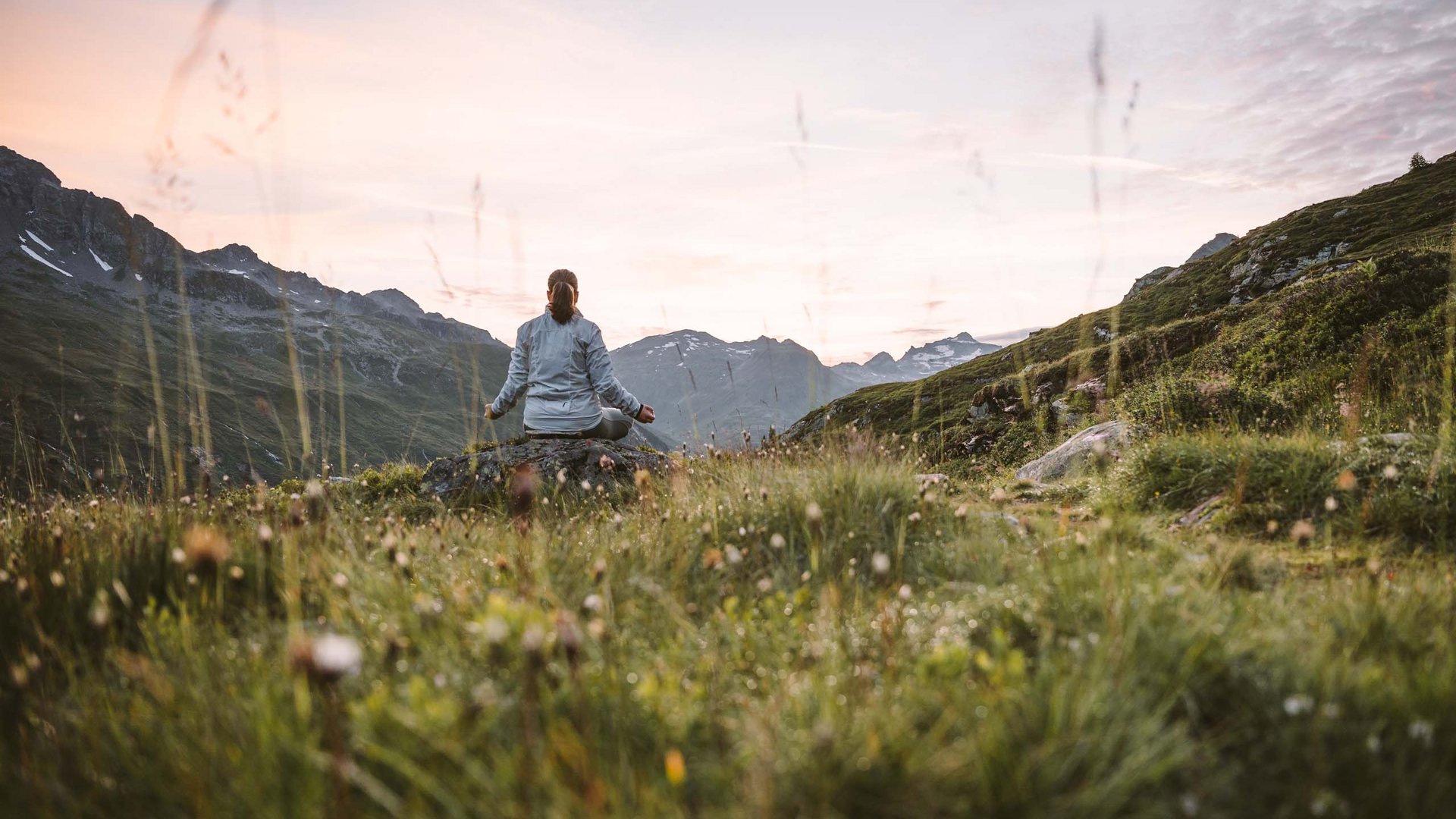 Alpine Urkraft im 4-Sterne-Superior-Hotel in Osttirol Person meditiert in den Bergen bei Sonnenuntergang