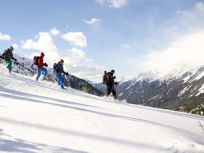 Benessere alpino al nostro albergo in Tirolo Quattro persone che fanno racchette da neve in montagna innevata con sole