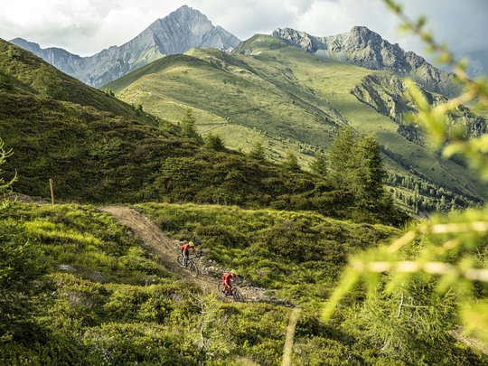 Mountain biking routes for all levels Two mountain bikers riding on a trail through green alpine hills