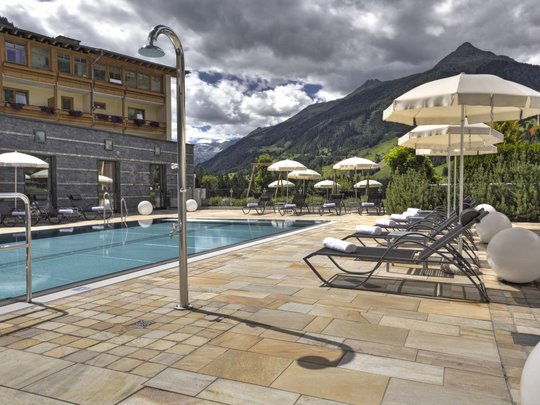 Wanderhotel in Osttirol mit Herz Poolbereich mit Liegestühlen und Sonnenschirmen vor Bergkulisse