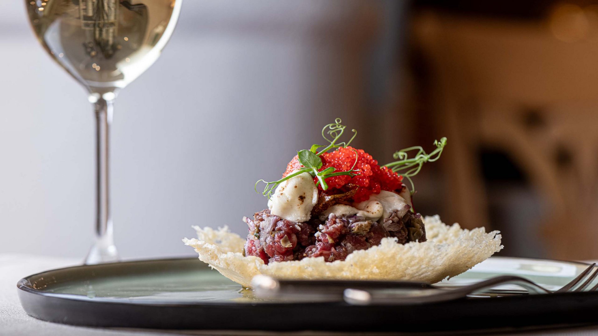 Jesacherhof: Gourmethotel in Österreich Gourmetgericht mit rohem Fleisch und Fischrogen auf knusprigem Teller mit Weinglas
